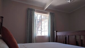 Una camera da letto con un letto, una finestra con tende, una testiera in legno e un lampadario.