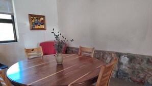 Un tavolo rotondo in legno con sedie, un vaso con fiori secchi, un cuscino rosso e un quadro appeso al muro.