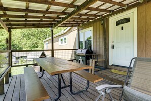 A covered patio with a wooden table and benches, a grill, and a chair. - Furnished Deck, Private Yard! Quaint Knoxville Gem (Knoxville)