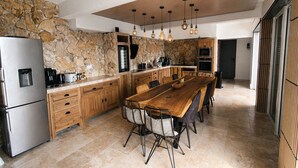 A modern kitchen with a stone backsplash, wooden cabinets, a stainless steel refrigerator, and a long wooden dining table with chairs. - Villa Ventoux - 100% Private - 2 steps from Avignon (Villeneuve-lès-Avignon)