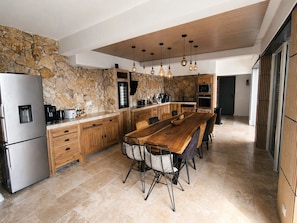 A modern kitchen with a stone backsplash, wooden cabinets, a stainless steel refrigerator, and a long wooden dining table with chairs. - Villa Ventoux - 100% Private - 2 steps from Avignon (Villeneuve-lès-Avignon)