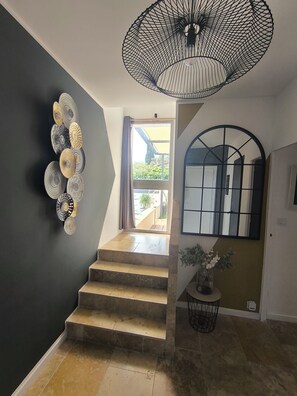 En trappa med modern design, en väggmonterad dekorativ lampa och en utsikt genom en öppen dörr.
