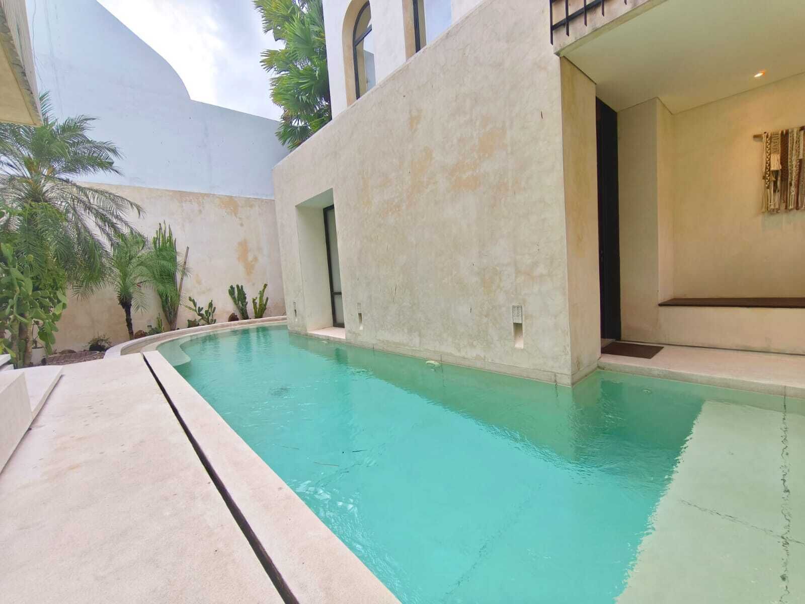 A swimming pool with a curved edge, surrounded by a low wall and palm trees.