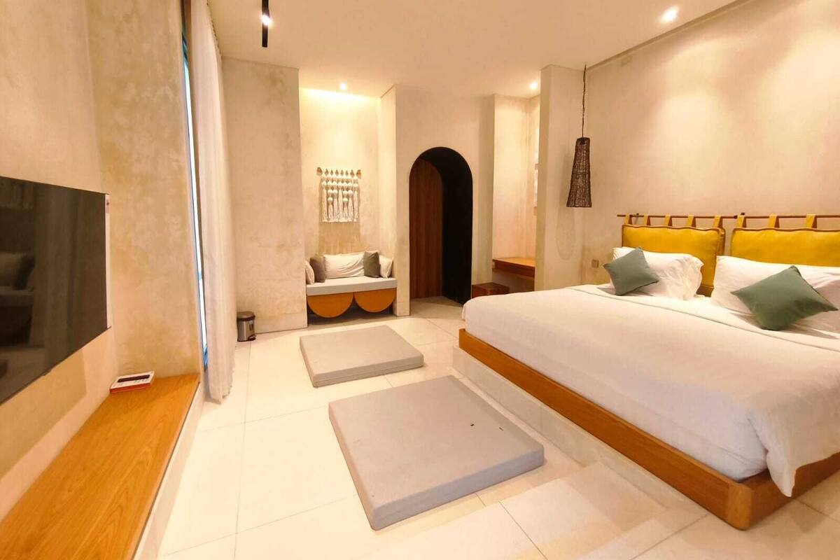 Une chambre moderne avec un grand lit, une télévision et un coin salon agrémenté de coussins.