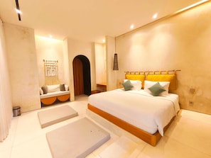 A bedroom with a large bed, a bedside table, a bench, and a door leading to another room. - Asteria Fajar Villa by ABM (Canggu)