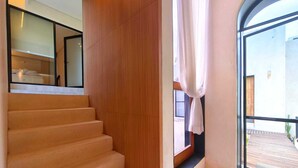 Un interior moderno con una escalera de madera, un ventanal con cortinas y vistas a una terraza exterior.