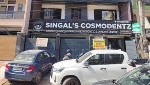 A building with a sign for 'Singal's Cosmopolitan Dental Clinic' and a parked white SUV. - Steam and pool  with entire Roof top best to relax (Gurugram)
