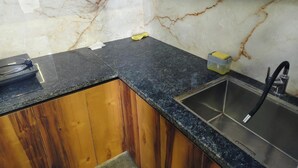 A kitchen with a marble backsplash, wooden cabinets, a black countertop, and a stainless steel sink. - Steam and pool  with entire Roof top best to relax (Gurugram)
