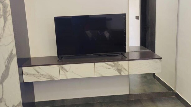 A modern room with a flat-screen TV on a marble and wood console, a door, and a light ceiling. - Steam and pool  with entire Roof top best to relax (Gurugram)