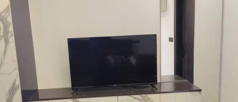 Quarto moderno com televisão de tela plana em console de mármore e madeira, uma porta e teto iluminado.