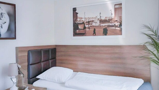 Ein ordentlich bezogenes Bett mit einem Holz-Kopfteil, ein Nachttisch mit einer Lampe und ein gerahmtes Bild an der Wand.