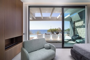 Ein modernes Interieur mit einer Couch, einem Bett und Blick aufs Meer durch eine Glastür.