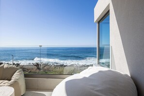 Ein Zimmer mit Meerblick, einem weißen Bett und einem beigefarbenen Sessel.