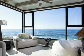 Ein modernes Wohnzimmer mit einem großen Fenster mit Blick auf den Ozean, einem Deckenventilator und einem einzigartigen, baumförmigen Couchtisch.