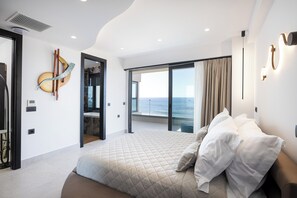 Une chambre moderne avec un grand lit, une vue sur la mer et une porte-fenêtre coulissante donnant sur un balcon.