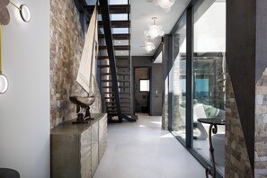 Un intérieur moderne avec un mur en pierre, un escalier et une porte vitrée donnant sur un balcon.