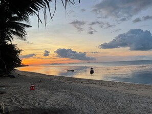 Ein Strand mit ruhigem Wasser, einem Boot und einem Sonnenuntergang.