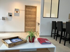 A modern room with a wooden door, a white table with a tray and magazine, a red potted plant, and black chairs. - Cosy house close to nature, 6/8 people, 10 min from FRAISPERTUIS park (La Bourgonce)