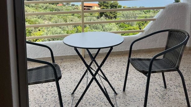 Un balcon avec une table et deux chaises, donnant sur une étendue d’eau et un espace verdoyant.