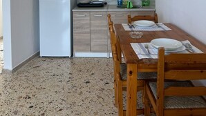 Une cuisine équipée d’un réfrigérateur, de meubles de rangement en bois, d’une table à manger avec des chaises et d’un luminaire suspendu.