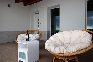 A wicker chair and a white table with a bottle and glasses on a balcony. - Villa in Marina Di Ragusa with 5 bedrooms sleeps 13 (Marina Di Ragusa)