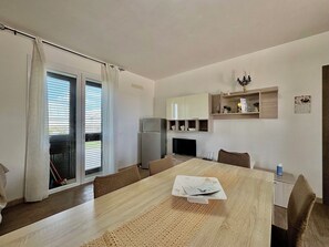 Una cucina moderna con zona pranzo, frigorifero, televisore e un piccolo ripiano con oggetti decorativi.
