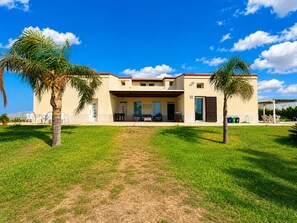 Una casa a due piani con un portico coperto, un prato e due palme.