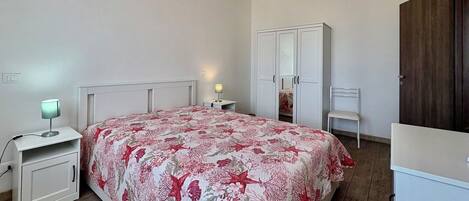 A bedroom with a bed, a nightstand, a desk, a chair, a wardrobe, and a mirror.