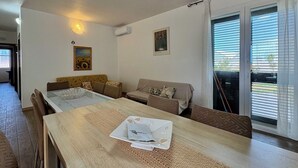 En moderne stue med spisebord, sofa og et stort vindue med persienner.