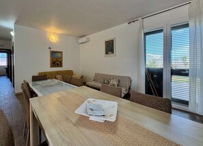 A modern living room with a dining table, sofa, and a large window with blinds. - Villa in Marina Di Ragusa with 5 bedrooms sleeps 13 (Marina Di Ragusa)