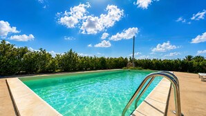 En klar blå pool med en metalstige, omgivet af frodig vegetation og en blå himmel.