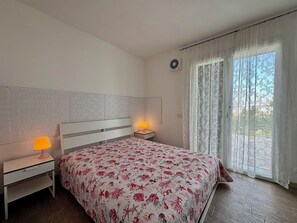 Une chambre à coucher comprenant un lit, deux tables de chevet avec des lampes, une fenêtre avec des rideaux et un climatiseur fixé au mur.