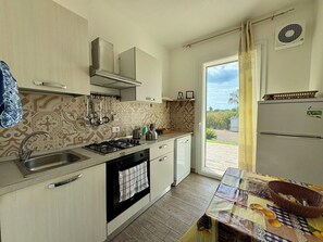 A compact kitchen with a gas stove, sink, and a view of the outdoors through a sliding door. - Villa in Marina Di Ragusa with 5 bedrooms sleeps 13 (Marina Di Ragusa)