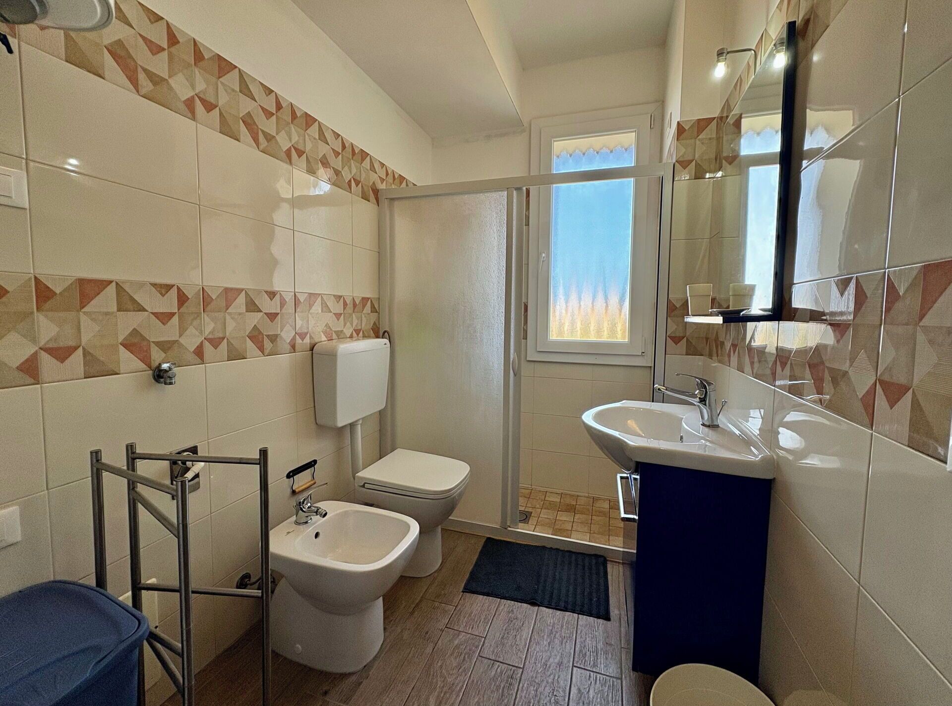 A bathroom with a toilet, bidet, and sink, a shower area, and a window with a view.