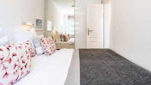 Una camera da letto con un letto, cuscini, un comodino, uno specchio e una porta che dà su un'altra stanza.