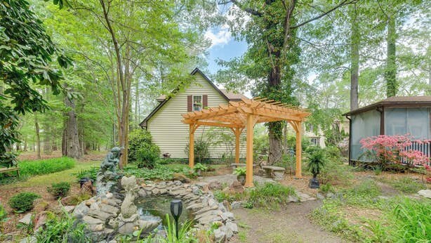 A garden with a wooden pergola, a stone pond, and a house with a gabled roof. - Pool Access! Cozy Couple's Getaway in Kilmarnock (Kilmarnock)