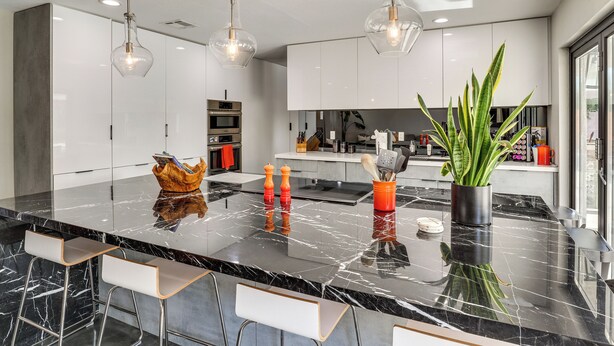 Een moderne keuken met een marmeren aanrechtblad, hanglampen en barstoelen.