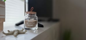 A clear glass jar with a wooden lid and a handle, labeled 'ENJOY THE LITTLE THINGS,' placed on a white surface. - Vacation apartment KWi 53 ground floor - "Ostwind" - Holiday apartment "Ostwind" with terrace and (Gelbensande)