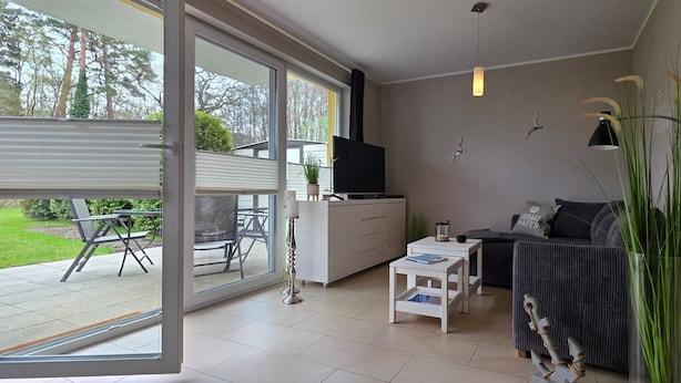 Una sala de estar moderna con un sofá, un televisor, una mesa de centro y una zona de comedor con sillas y una mesa.