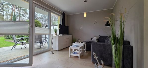 A modern living room with a sofa, a TV, a coffee table, and a dining area with chairs and a table. - Vacation apartment KWi 53 ground floor - "Ostwind" - Holiday apartment "Ostwind" with terrace and (Gelbensande)