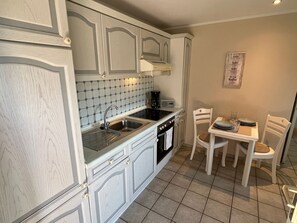 Eine Küche mit weißen Schränken, einer gefliesten Spritzschutzwand, einem Herd und einem Essbereich mit Tisch und Stühlen.