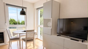 Ein modernes Wohnzimmer mit Flachbildfernseher, weißen Möbeln und großen Fenstern.