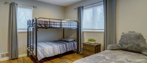 A room with a bunk bed, a single bed, a small bedside table with a plant, and a ceiling fan.