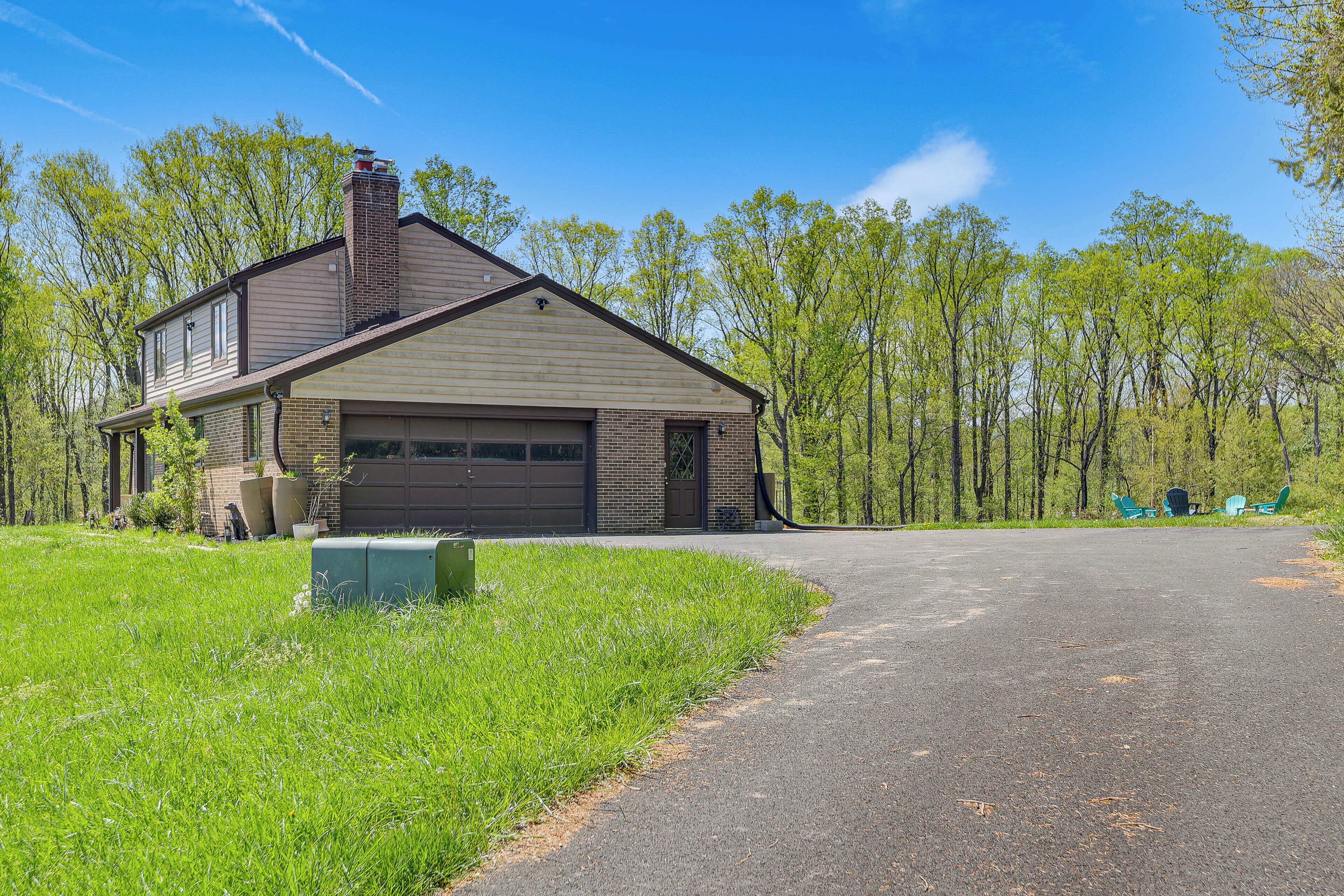 A two-story house with a garage, a chimney, and a driveway leading to a green lawn.