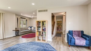 Un salon avec un canapé, un fauteuil bleu, une bibliothèque et un tapis rouge.