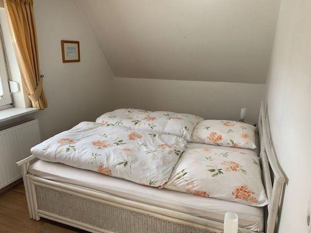 Et lille værelse med en enkeltseng, skrå vægge, en radiator og et vindue med gardiner.