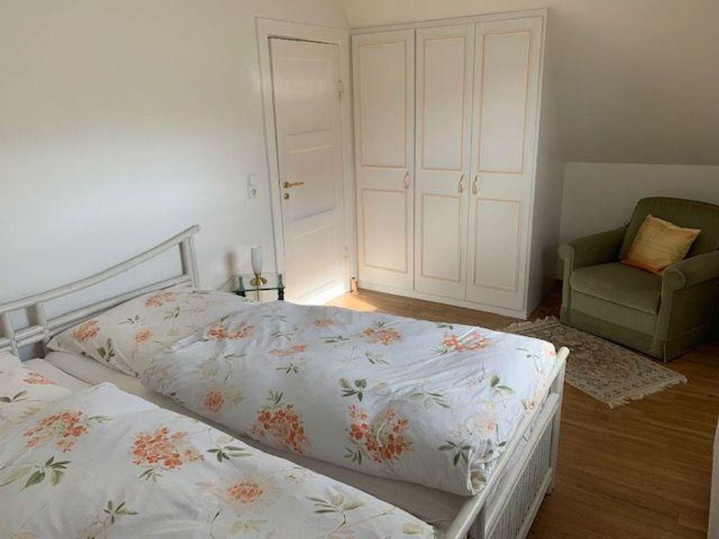 A bedroom with two beds, a wardrobe, a chair, and a nightstand.