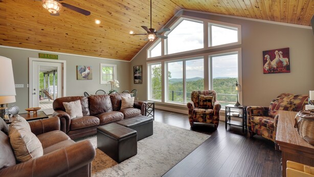 A spacious living room with leather sofas, a large window offering a view, and a ceiling fan. - Hot Tub & View! 'Lakehouse Lookout' Byrdstown Home (Byrdstown)