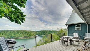 A deck with outdoor furniture overlooking a river, a small building with a green roof, and a view of a forested landscape. - Hot Tub & View! 'Lakehouse Lookout' Byrdstown Home (Byrdstown)
