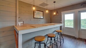 A kitchen with wooden walls, a bar counter, stools, pendant lights, and a window with a view. - Hot Tub & View! 'Lakehouse Lookout' Byrdstown Home (Byrdstown)
